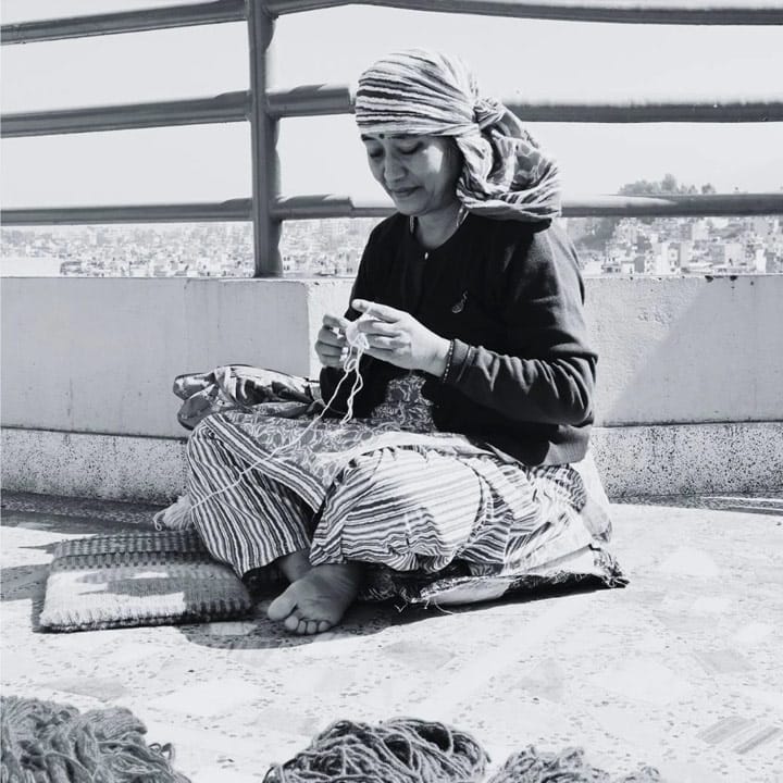 Artisane népalaise confectionnant à la main une création en laine feutrée sur un toit avec vue sur Katmandou. Fabrication artisanale pour Gry & Sif.