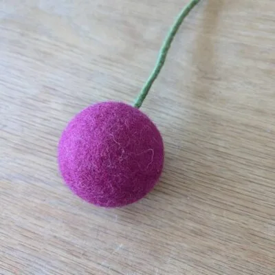 Fleur boule en feutre XL cerise de Gry & Sif sur surface en bois