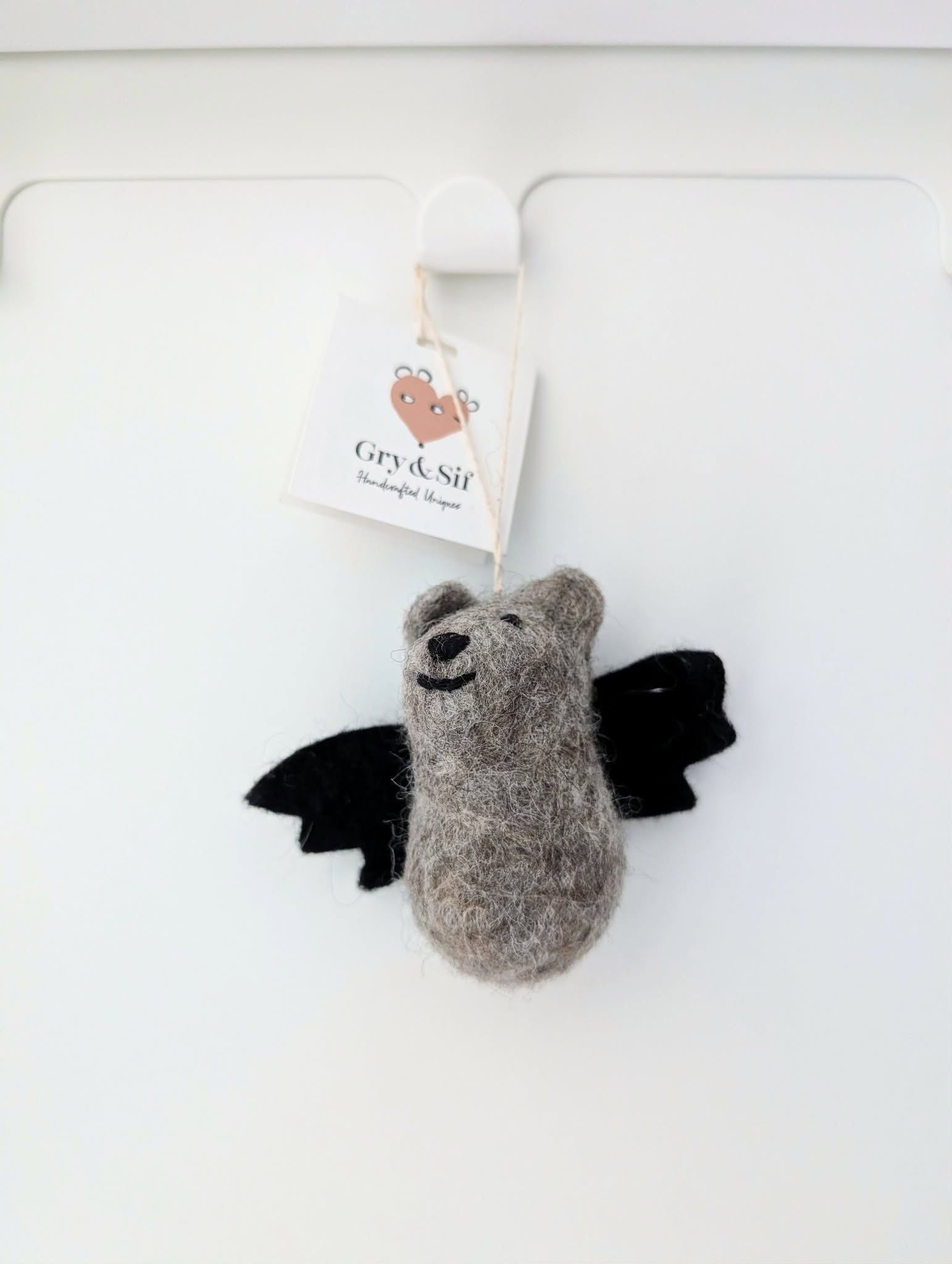 Chauve-souris grise en feutre Gry & Sif suspendue à une patère sur un mur blanc