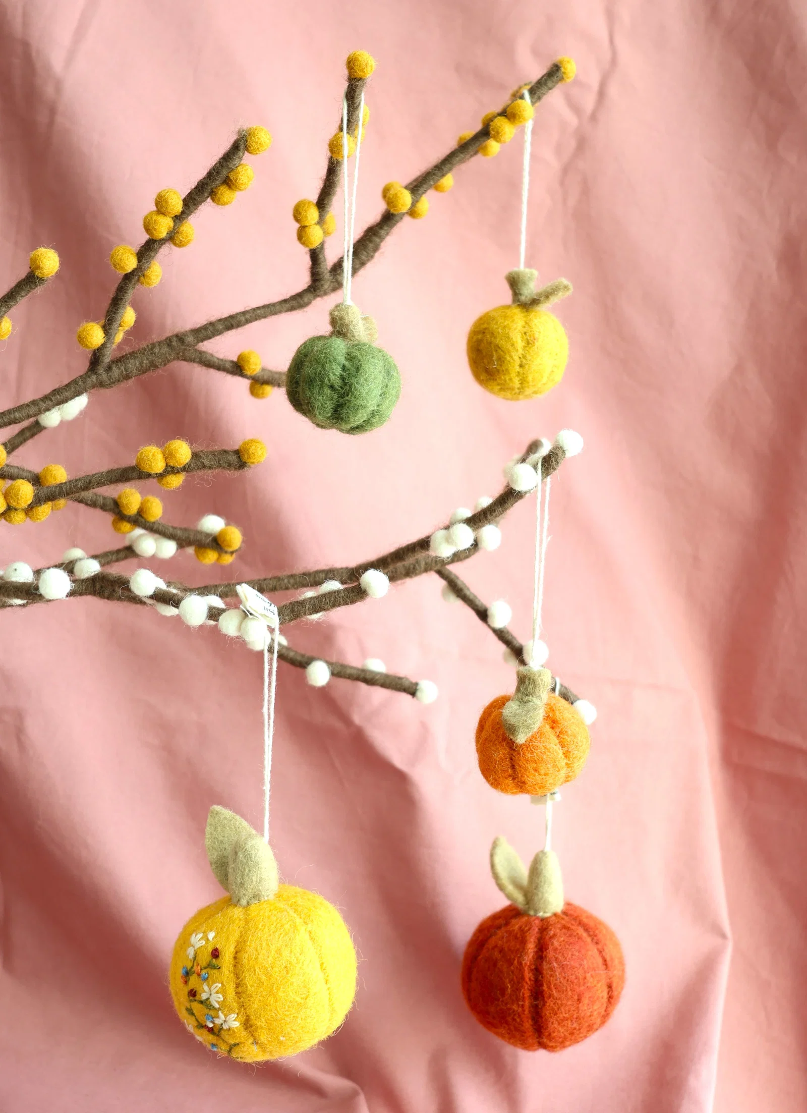 Citrouilles en feutre verte, jaune et orange Gry & Sif suspendues à des branches décorées de baies en laine